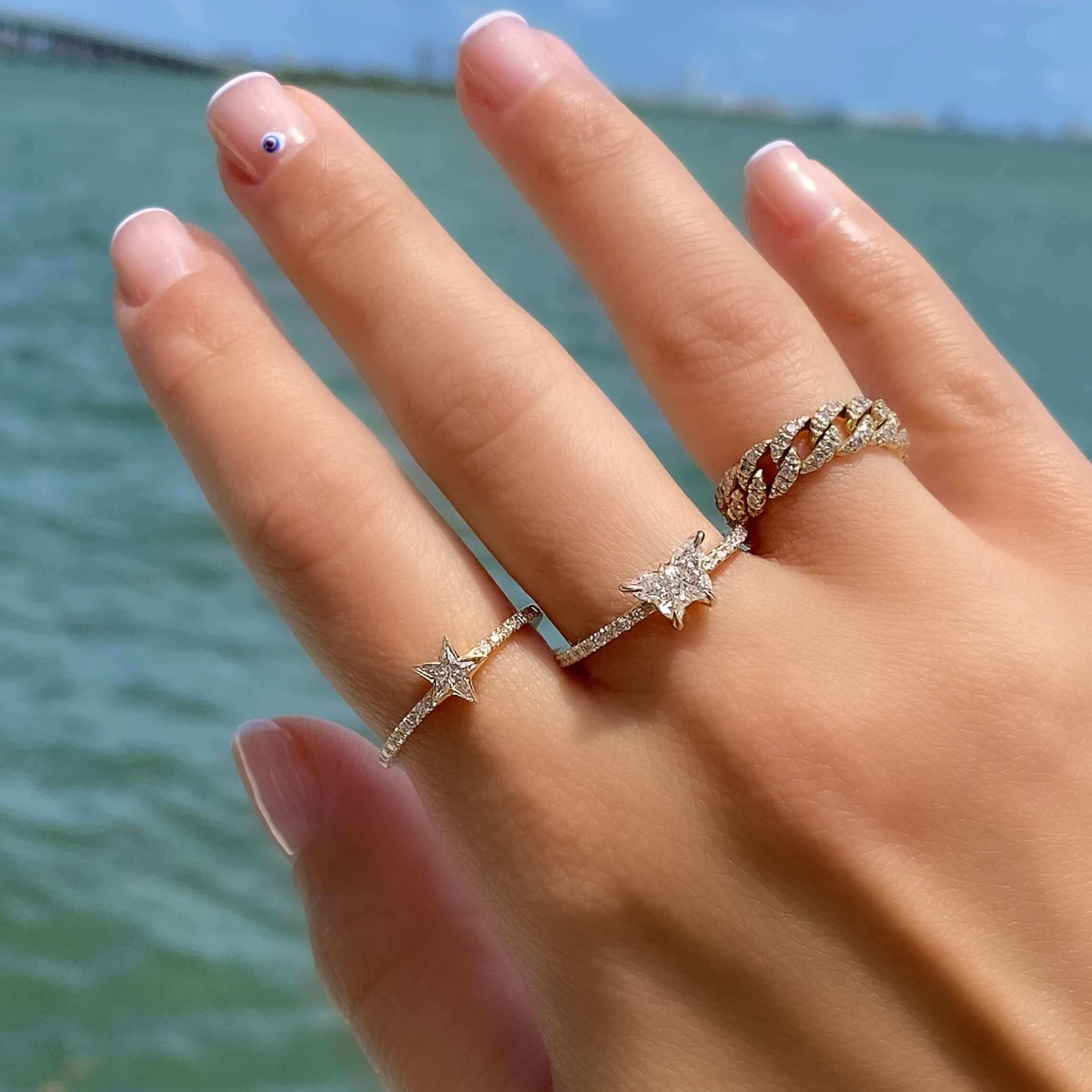 Elegant hand showcasing star-shaped diamond rings with a beach backdrop, luxury jewelry from our exclusive collection.