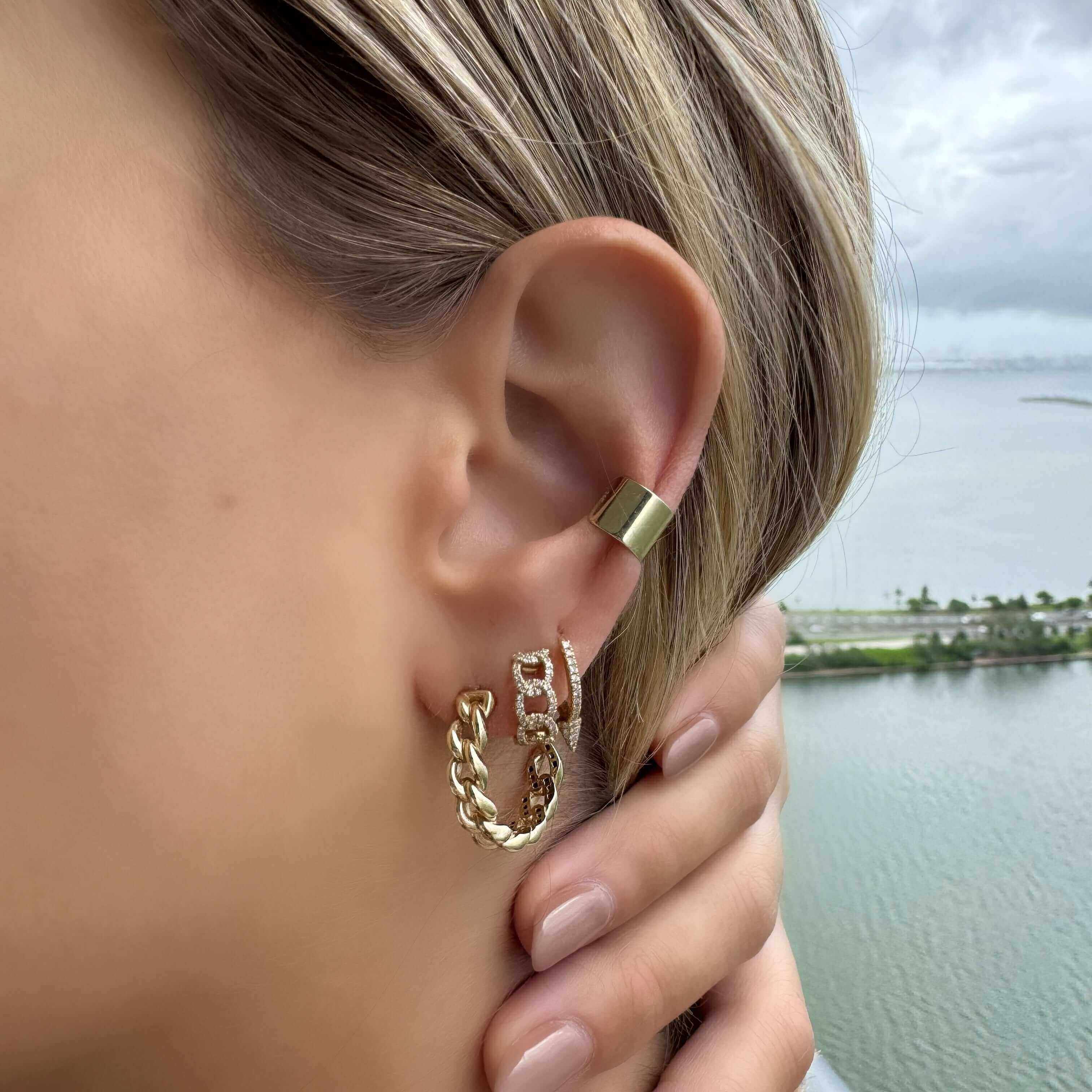 Close-up of a woman wearing stylish gold earrings with a chain design, by a scenic water view.