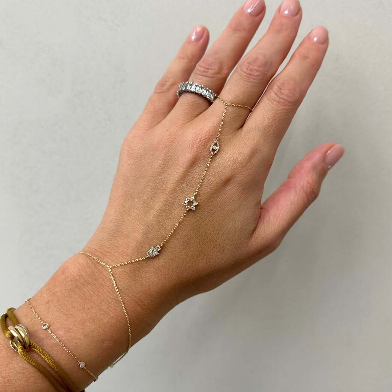 Elegant hand chains featuring a gold design with stars and hamsa charms, adorned on a woman's hand.