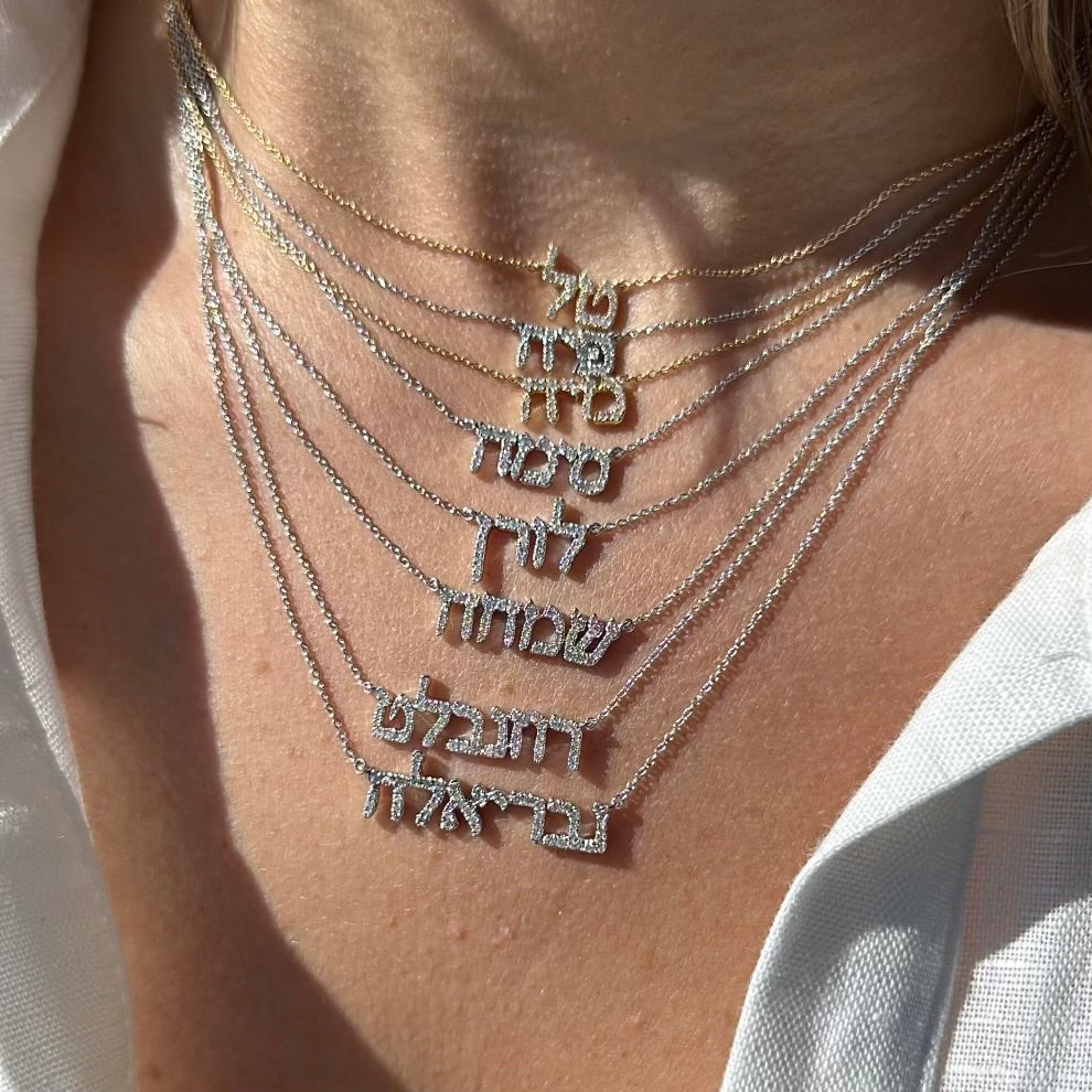 Close-up of layered Hebrew personalized necklaces in gold and silver, showcasing unique name designs.