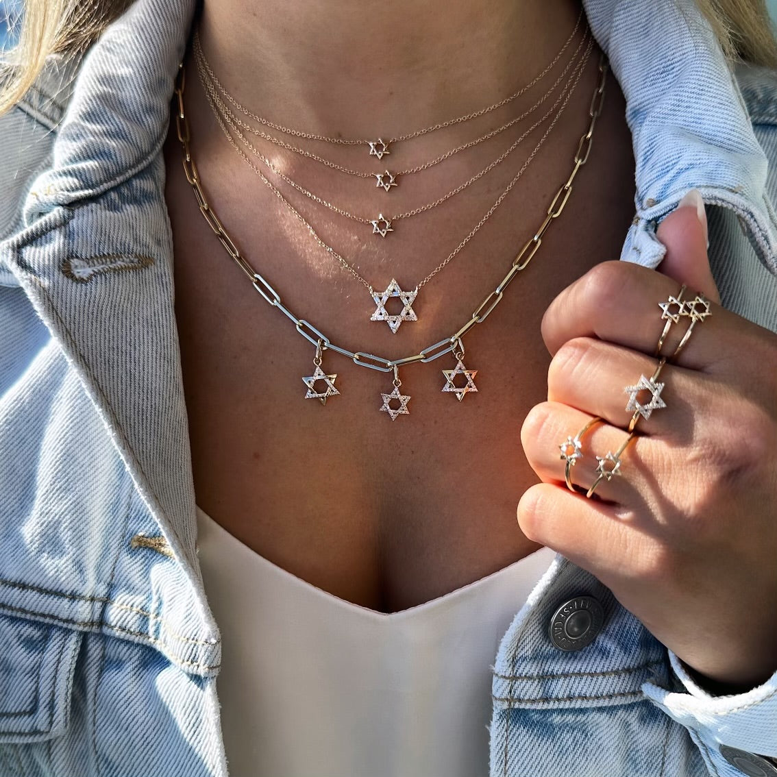 Elegant jewelry featuring multiple Star of David pendants and rings, styled with a denim jacket.