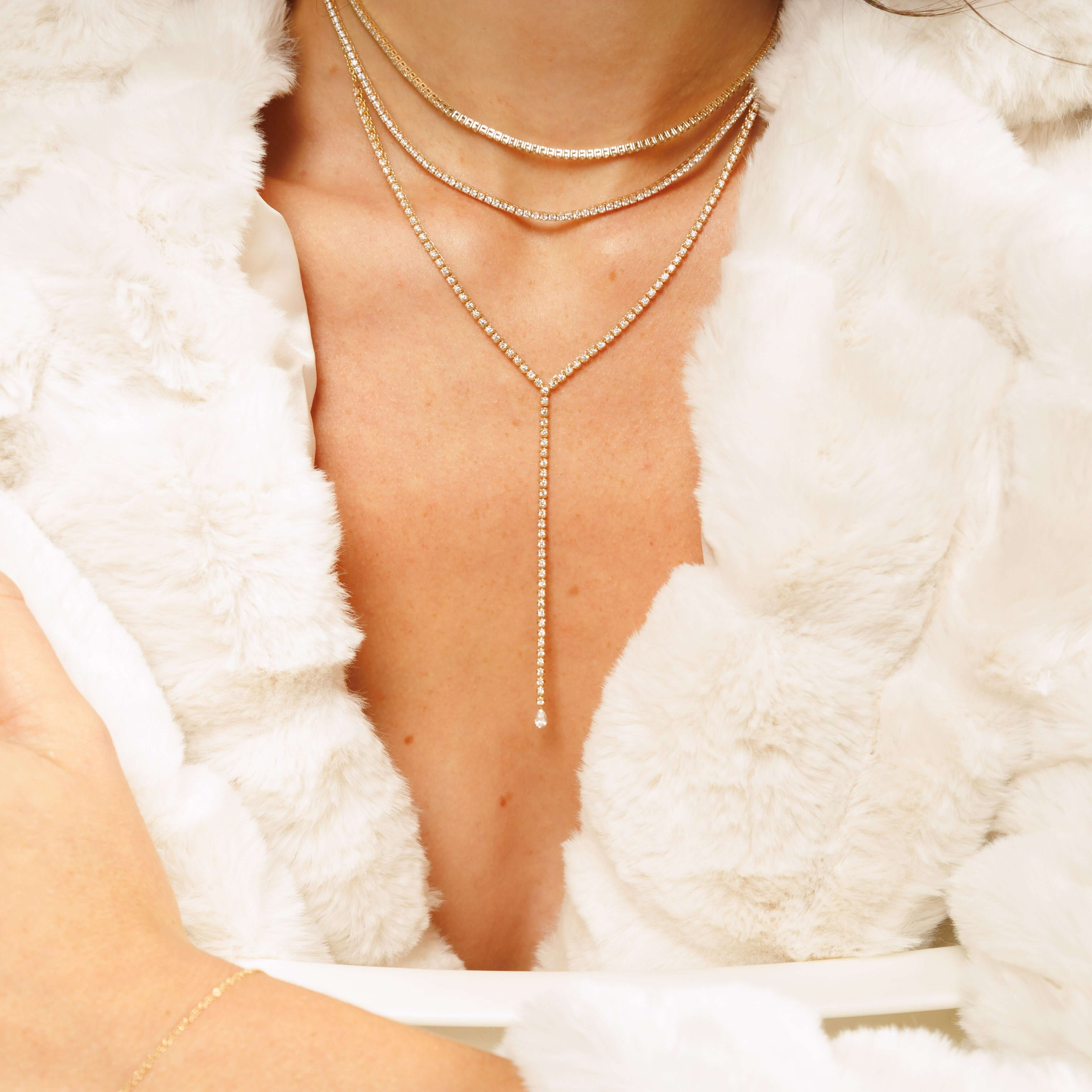 Elegant tennis necklaces layered on a model's neck, showcasing sparkling details against a soft, white fur backdrop.