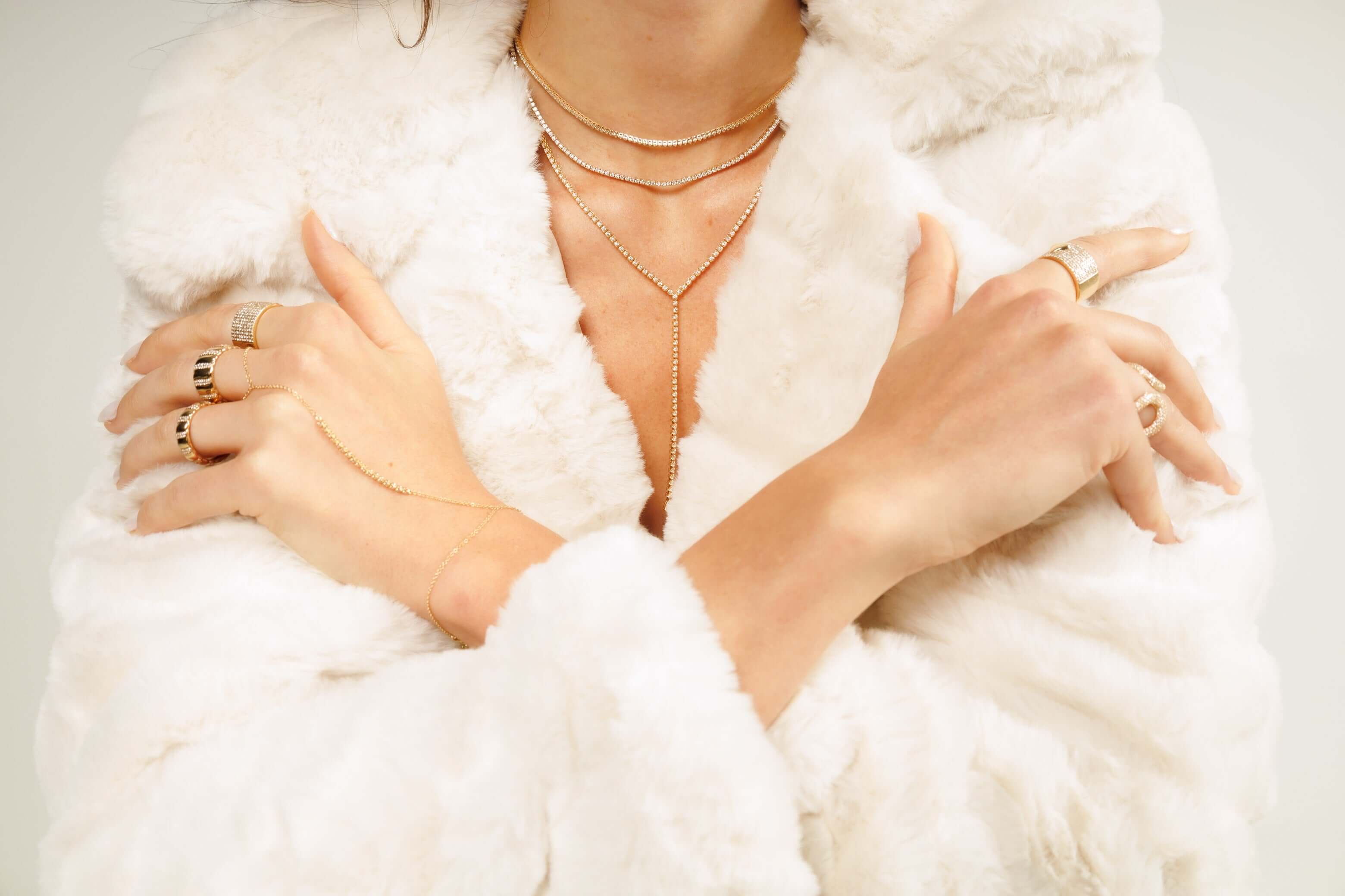 Elegant jewelry display with layered necklaces and rings against a soft, white faux fur coat backdrop.