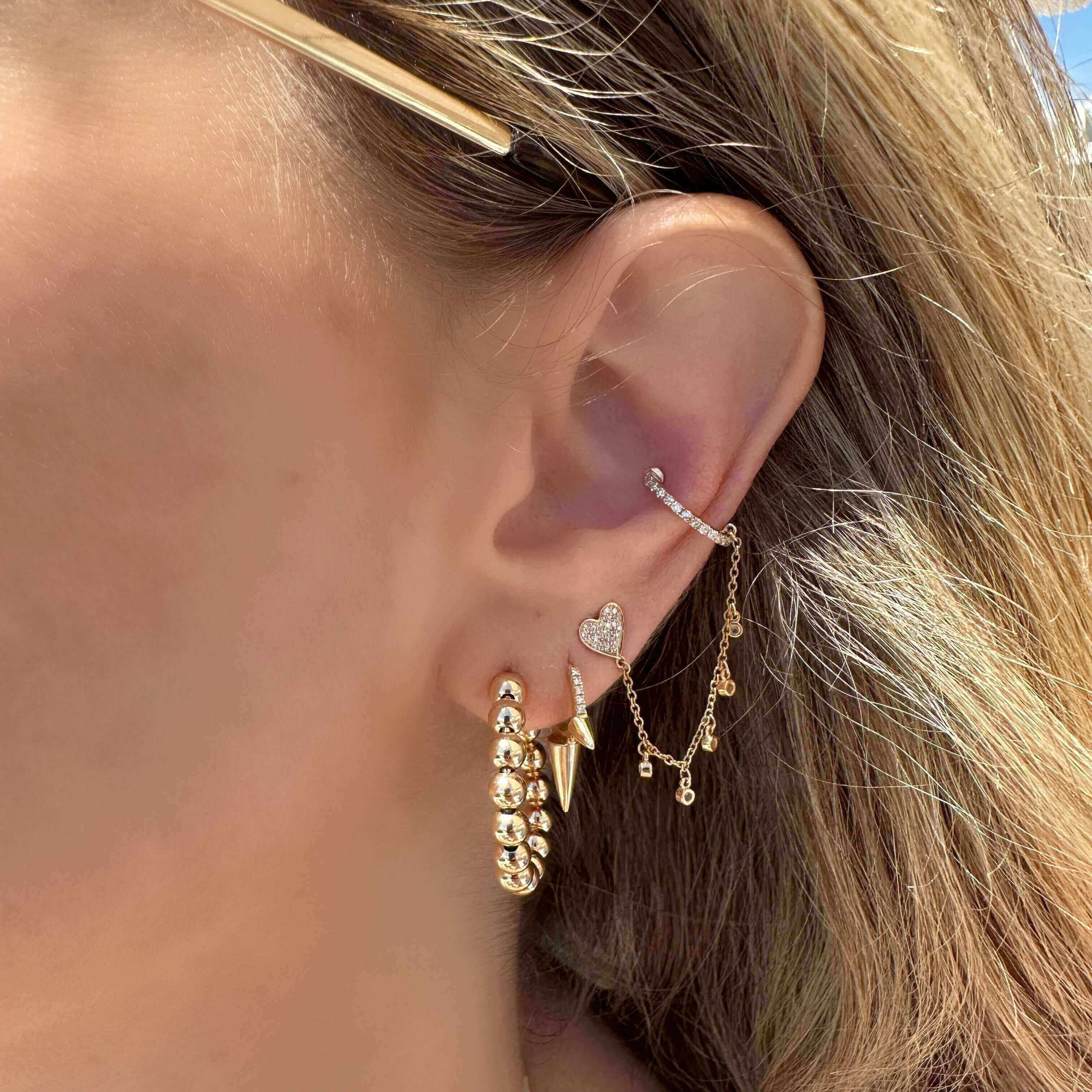 Woman's ear adorned with gold and diamond earrings from our jewelry collection, showcasing heart pendant and chain detail.