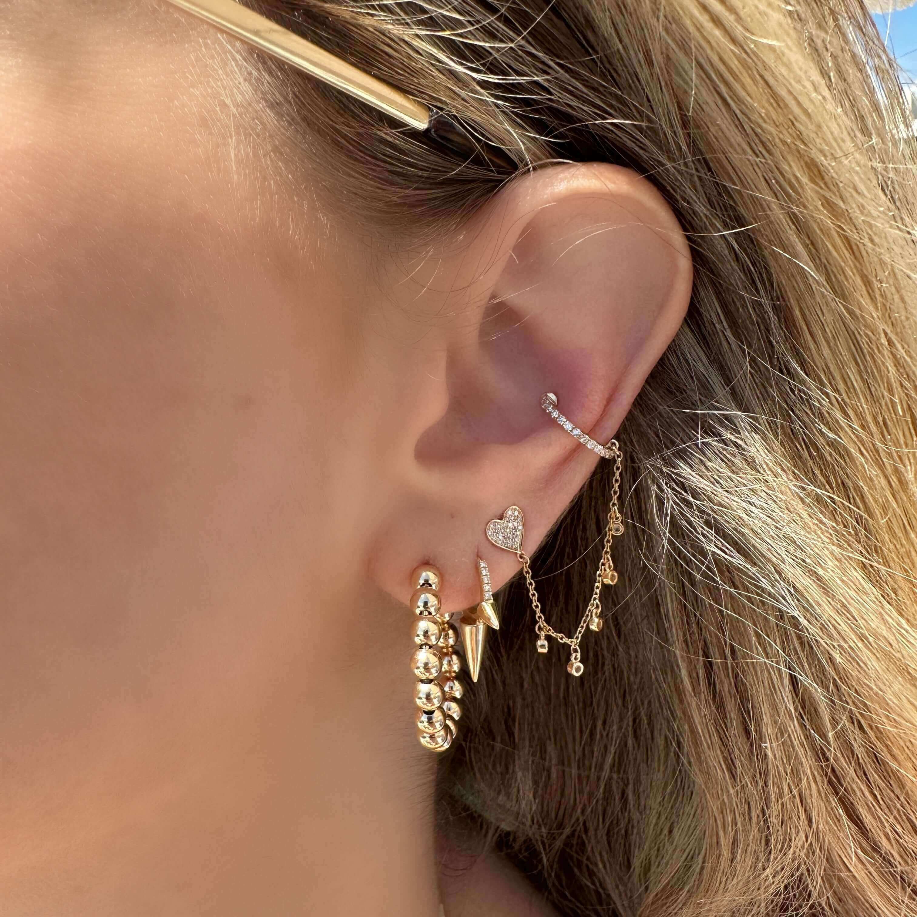 Woman's ear adorned with gold and diamond earrings from our jewelry collection, showcasing heart pendant and chain detail.