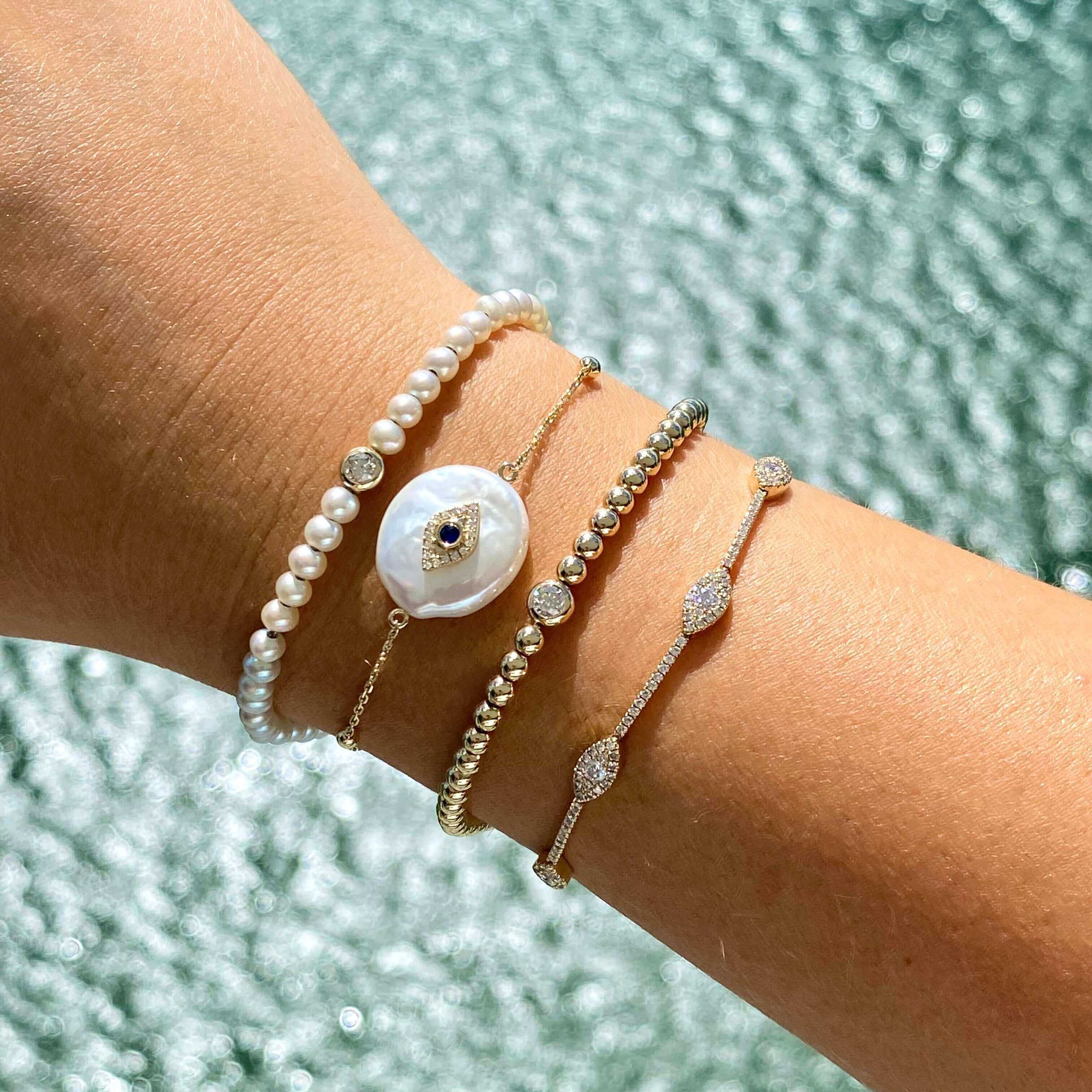 Elegant stack of luxury bracelets including pearls and gold beads by our jewelry brand, showcased on wrist with shimmering background.