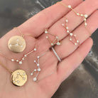 Hand holding constellation-inspired gold and silver necklaces with diamond accents.