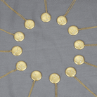 Gold constellation pendant necklaces arranged in a circle on a gray fabric background.