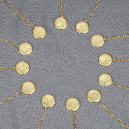 Gold constellation pendant necklaces arranged in a circle on a gray fabric background.