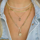 Woman wearing layered gold necklaces with lock and seashell pendants, styled with a denim jacket.