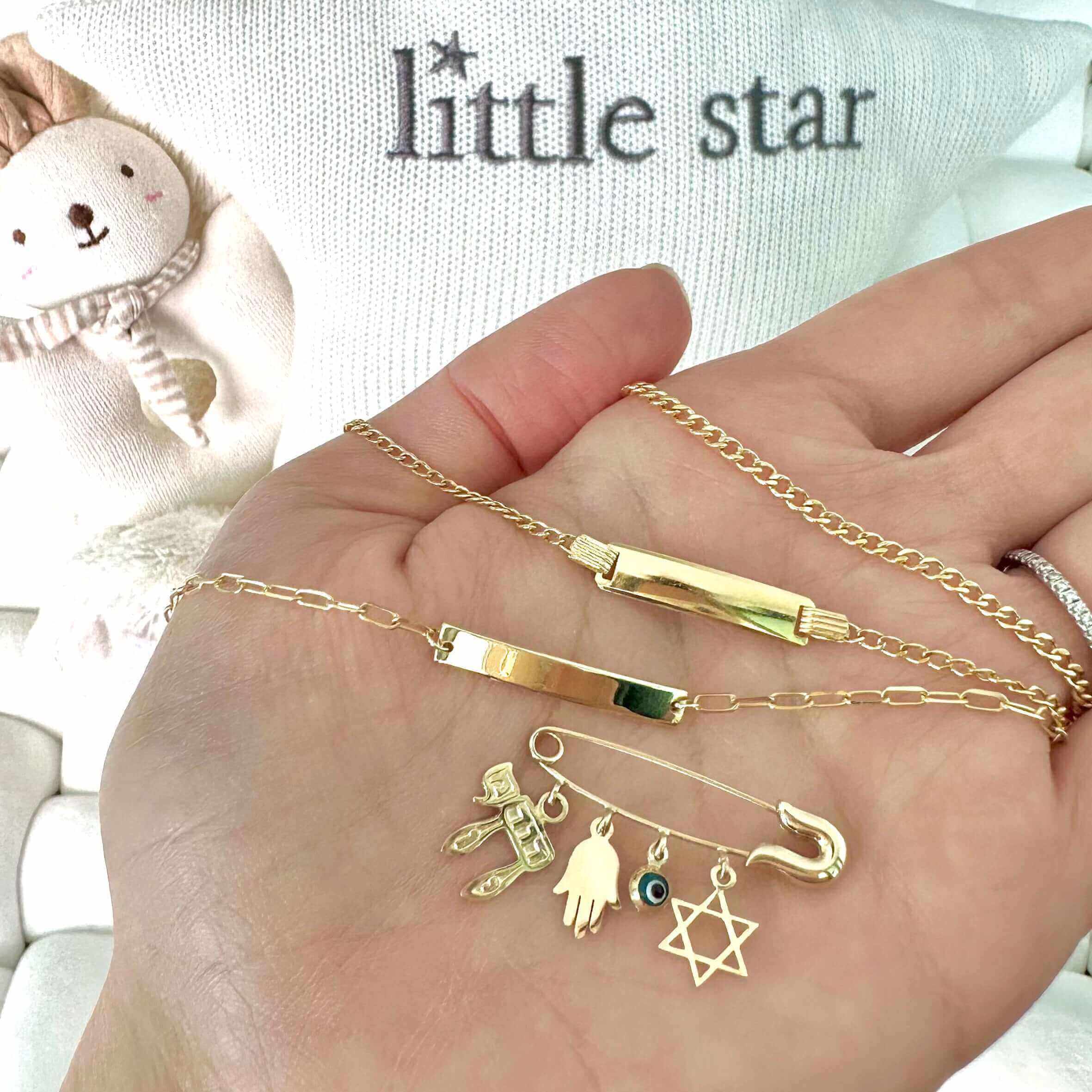 Gold jewelry with charms from Little Star jewelry brand in an open hand with a bear plush in the background