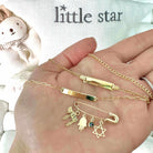 Gold jewelry with charms from Little Star jewelry brand in an open hand with a bear plush in the background