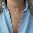 Layered silver necklaces with Jewish symbols on a woman wearing a light denim shirt