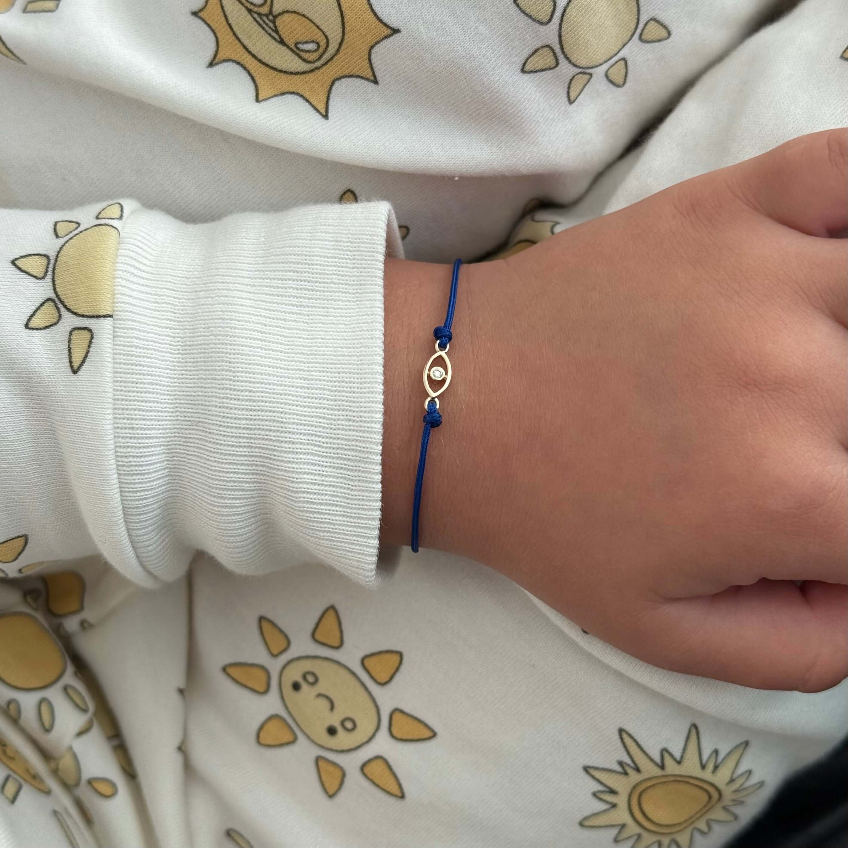 14K gold evil eye baby bracelet with blue cord, worn on a child's wrist, featuring diamond accents.