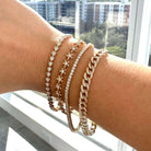 a hand adorned with multiple 14K gold and diamond bracelets against a bright window backdrop