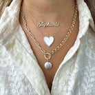 Woman wearing layered gold and silver necklaces with personalized name pendant, heart charm, and a pearl pendant, showcasing our jewelry brand's elegance.