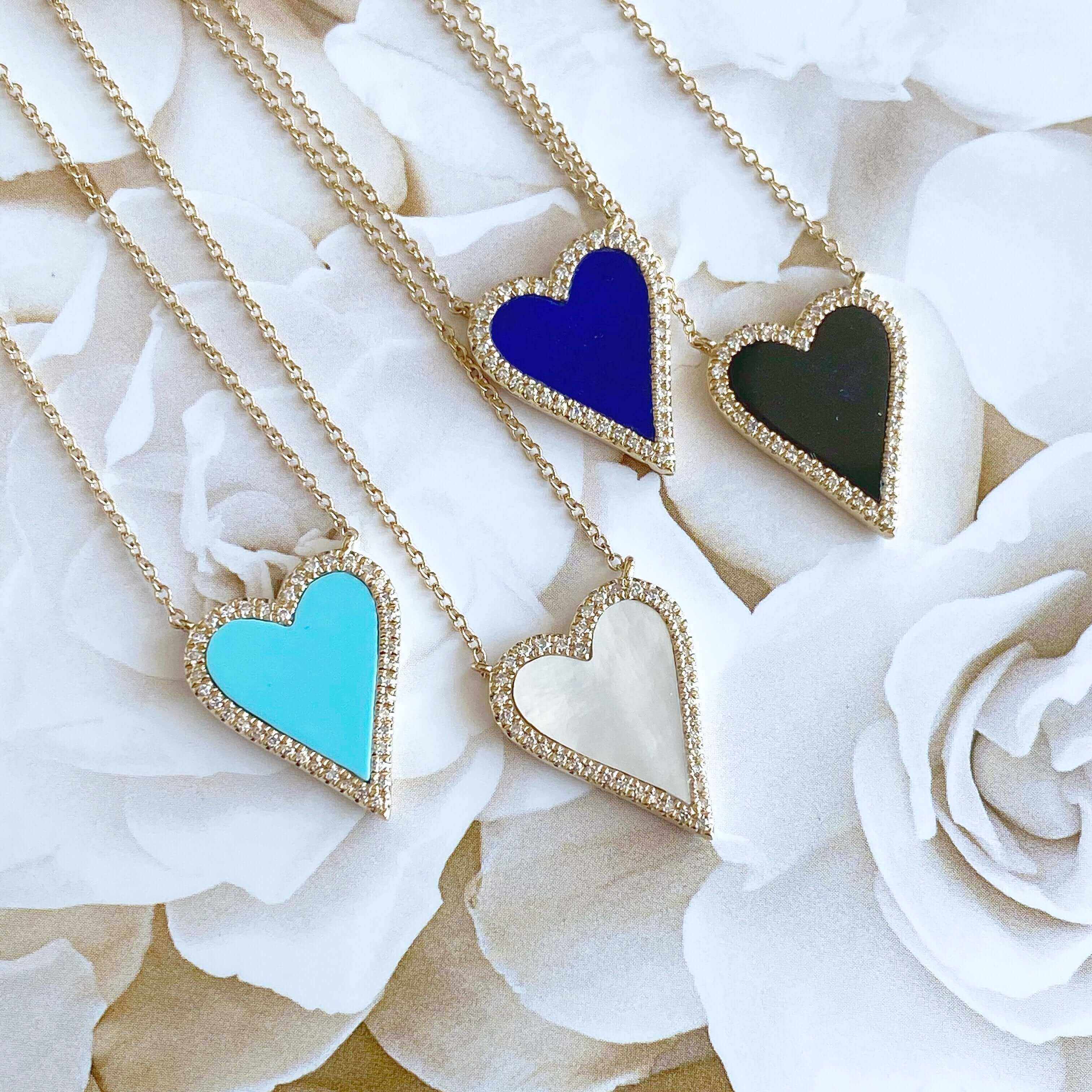 Gold heart necklaces with colorful enamel pendants on floral background reflecting our luxury jewelry collection.