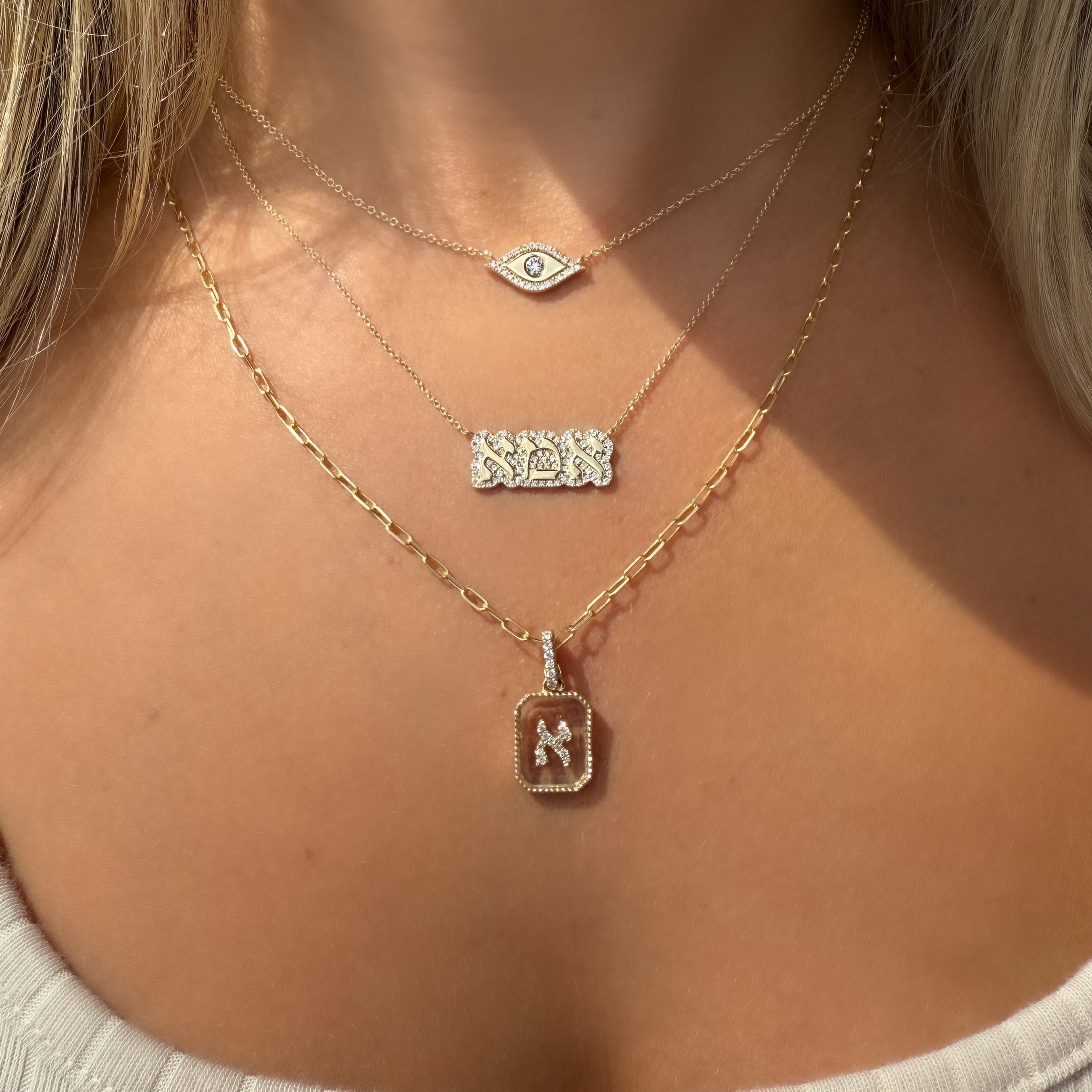 Woman wearing layered necklaces including 14K gold diamond Hebrew initial pendant on crystal with enhancer clasp.