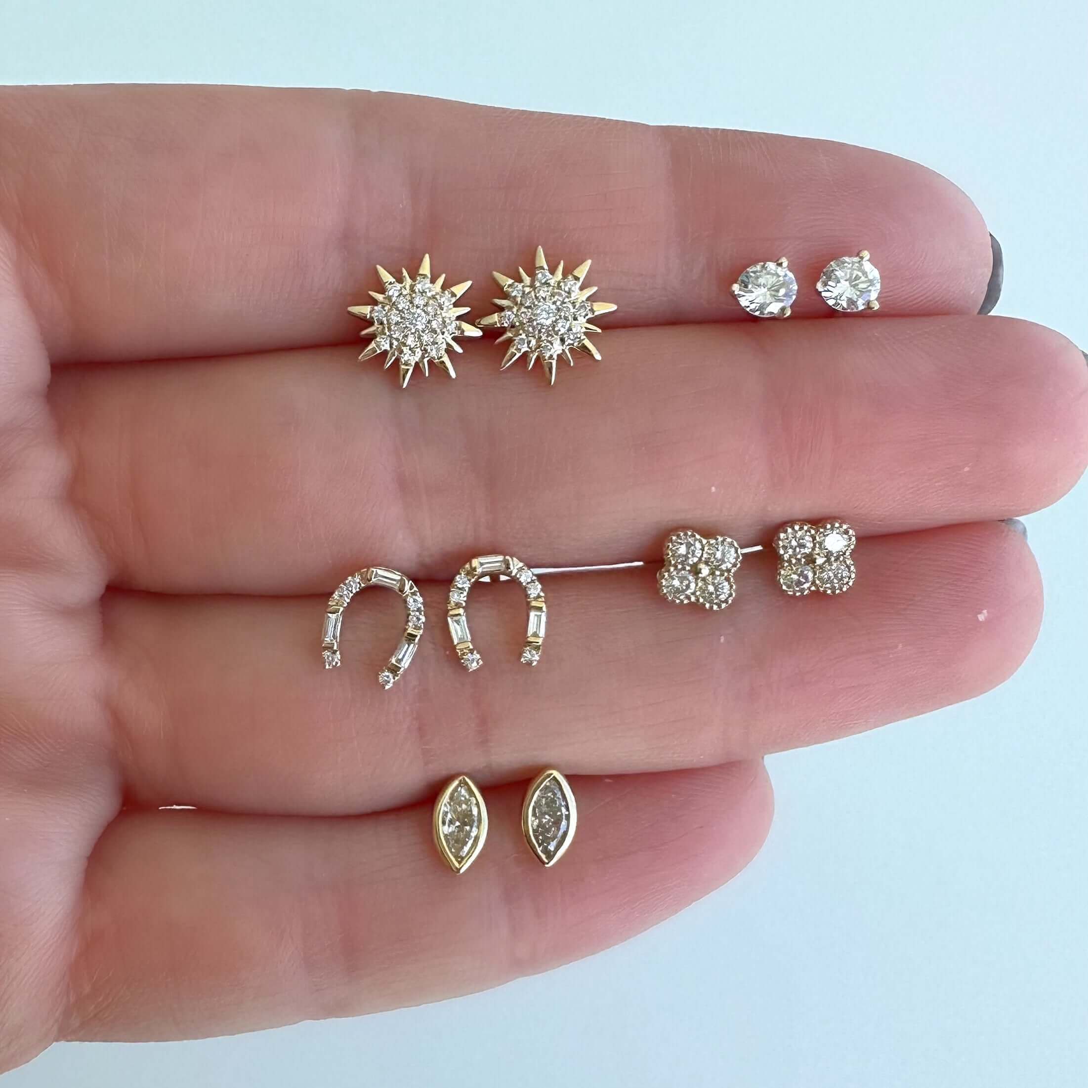 Hand holding various gold and diamond stud earrings from our jewelry collection, showcasing different elegant designs.