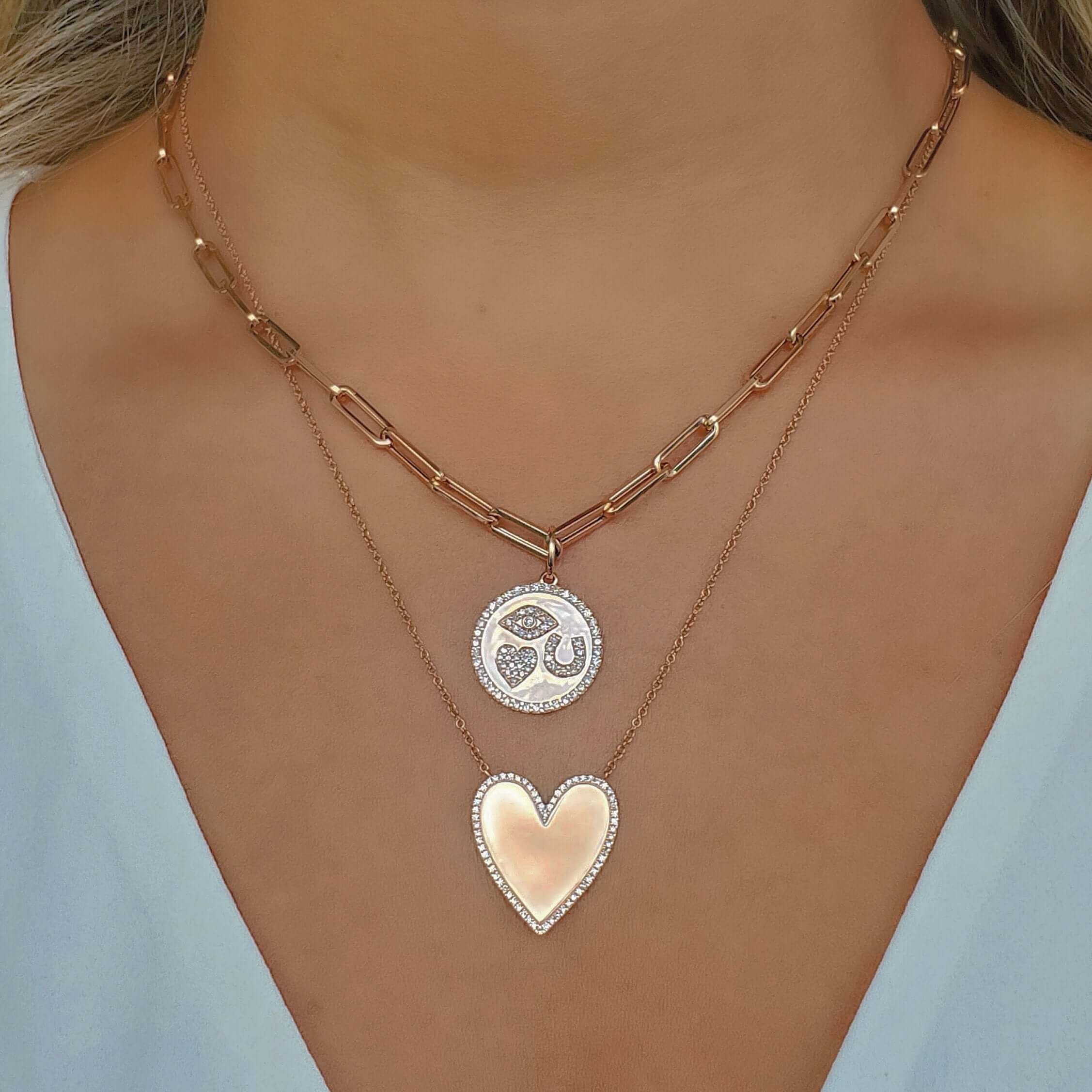 Woman wearing layered necklaces with heart and circular pendant, showcasing our elegant jewelry collection in rose gold.