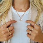 Woman wearing gold layered necklaces with coin pendant and multiple gold rings from [Your Jewelry Brand Name]