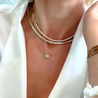 Woman wearing layered gold necklaces and white blazer showcasing luxury jewelry brand elegance