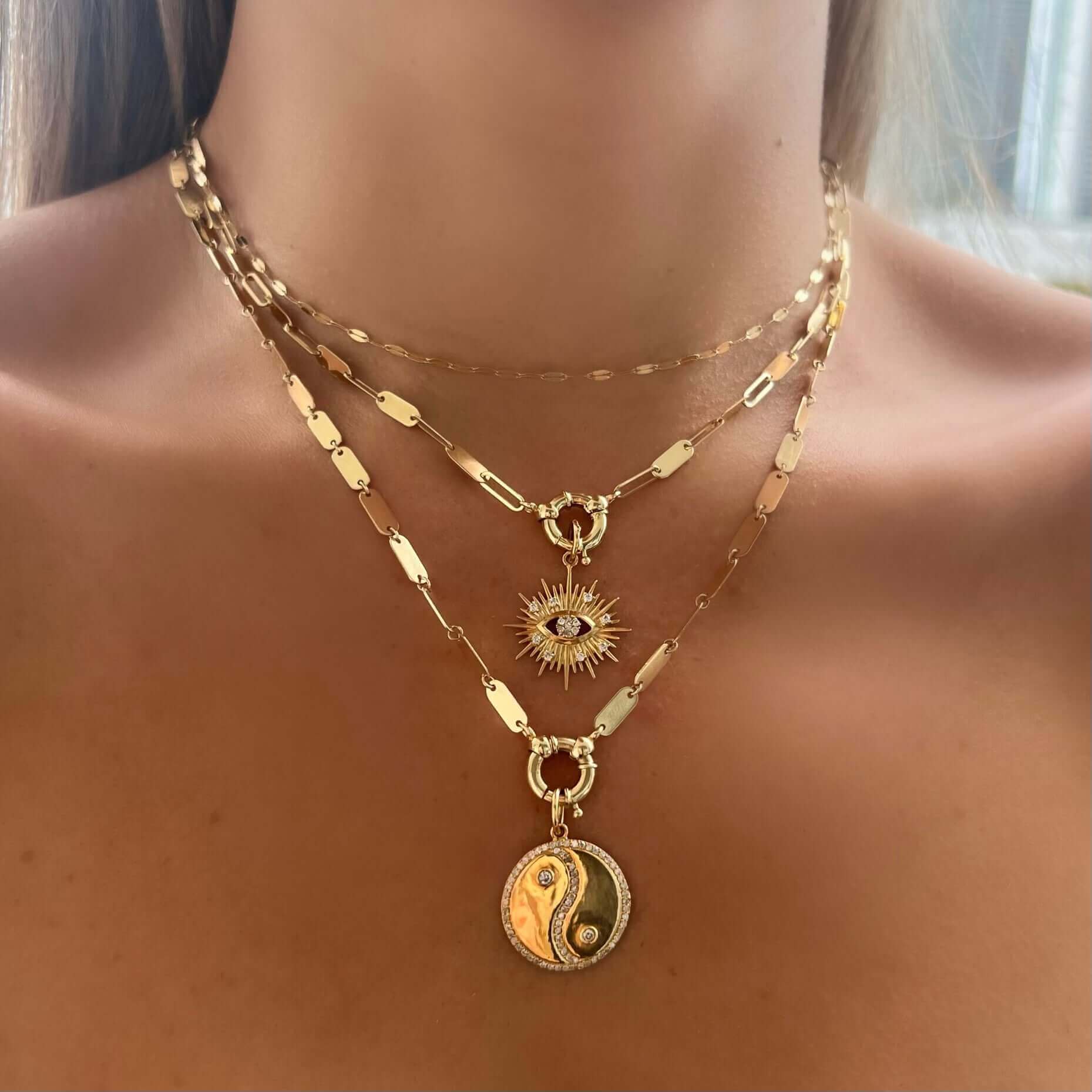 Woman wearing layered gold necklaces with sun and yin yang pendants, from our exclusive jewelry collection