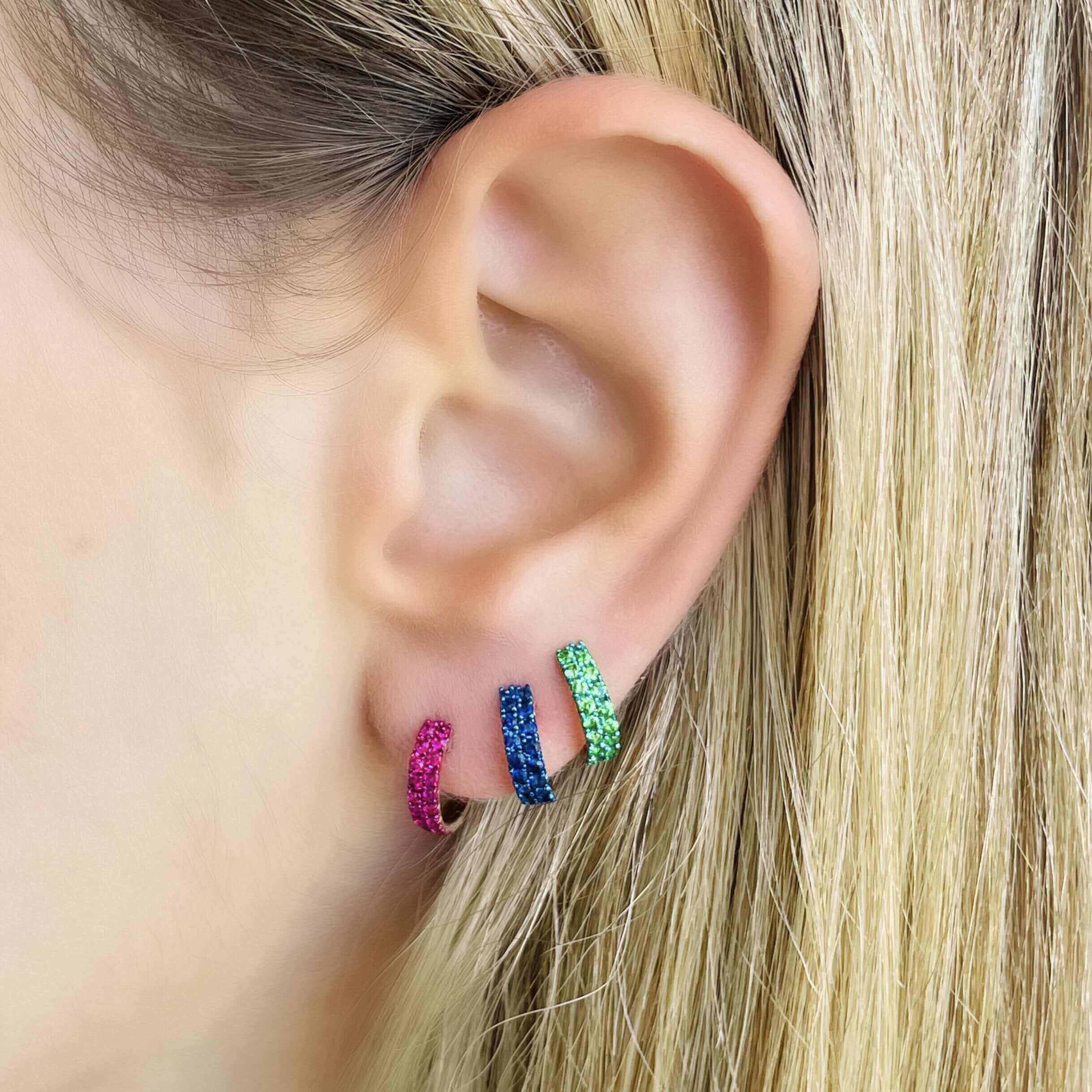 Woman wearing vibrant gemstone hoop earrings in pink, blue, and green colors from our exclusive jewelry collection