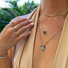 Woman wearing elegant jewelry including gold rings and layered necklaces by tropical plants