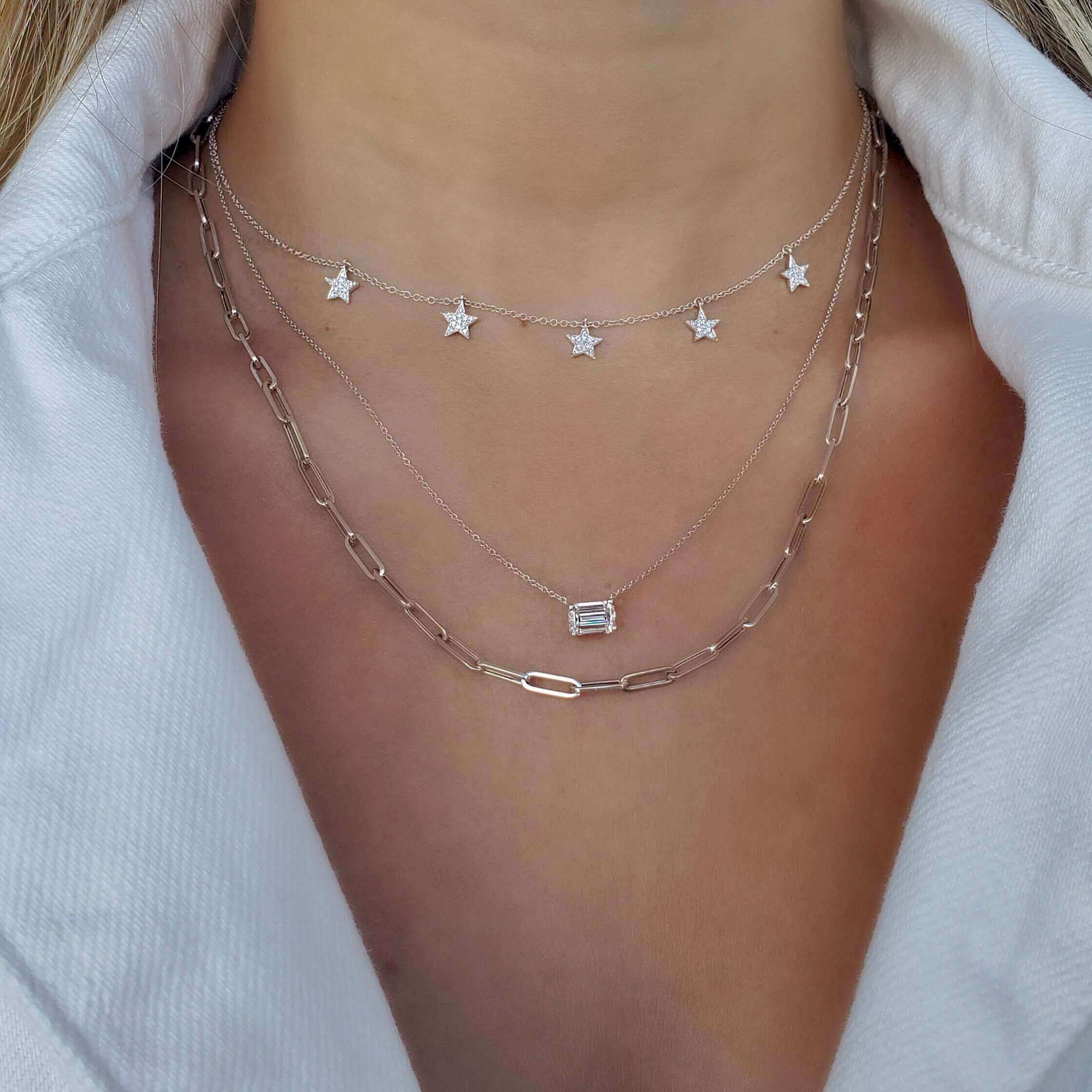 Woman wearing layered silver necklaces with stars and geometric pendant, showcasing our brand's elegant jewelry collection.