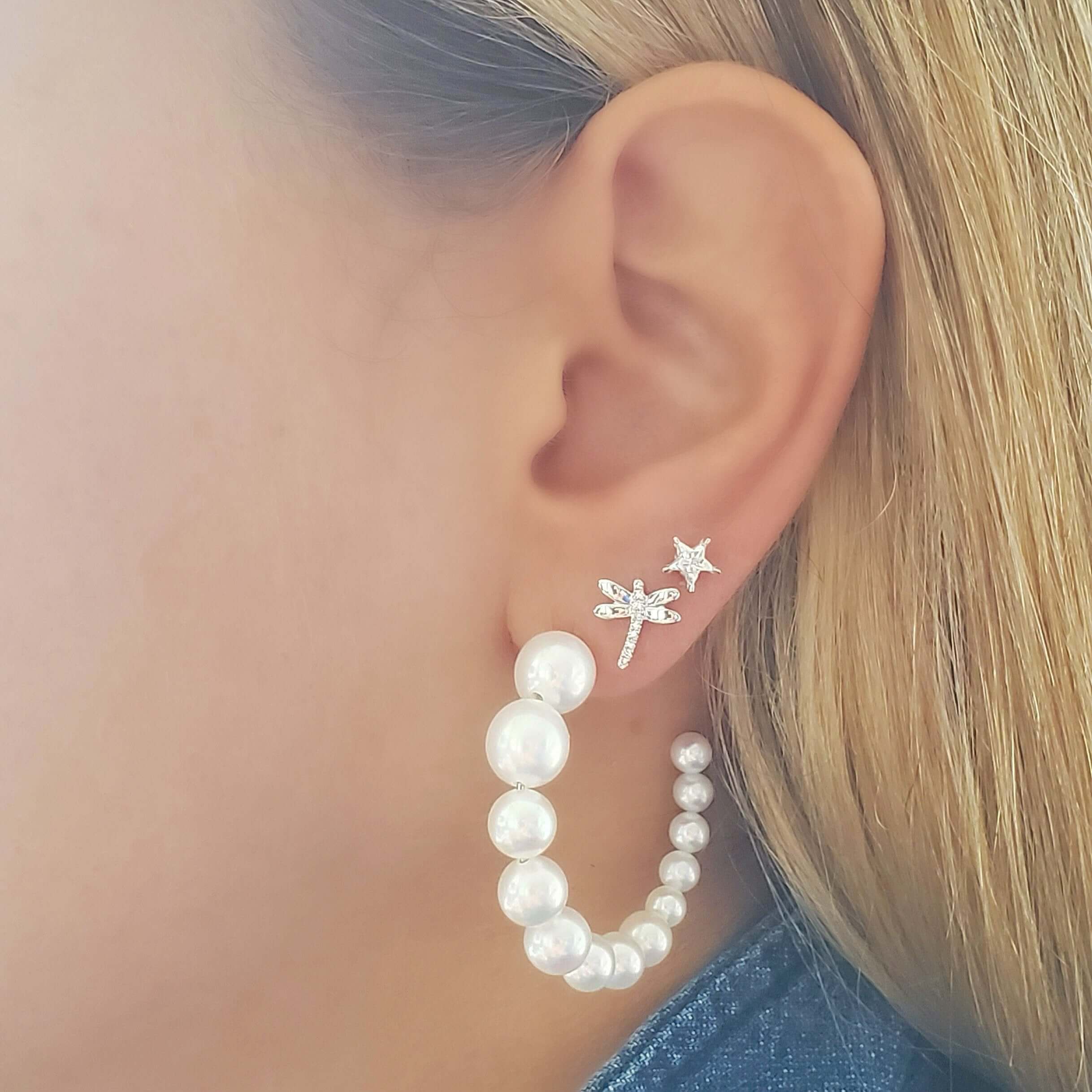 Woman wearing elegant pearl hoop earrings with delicate diamond-studded star and palm tree ear studs, showcasing our jewelry collection.