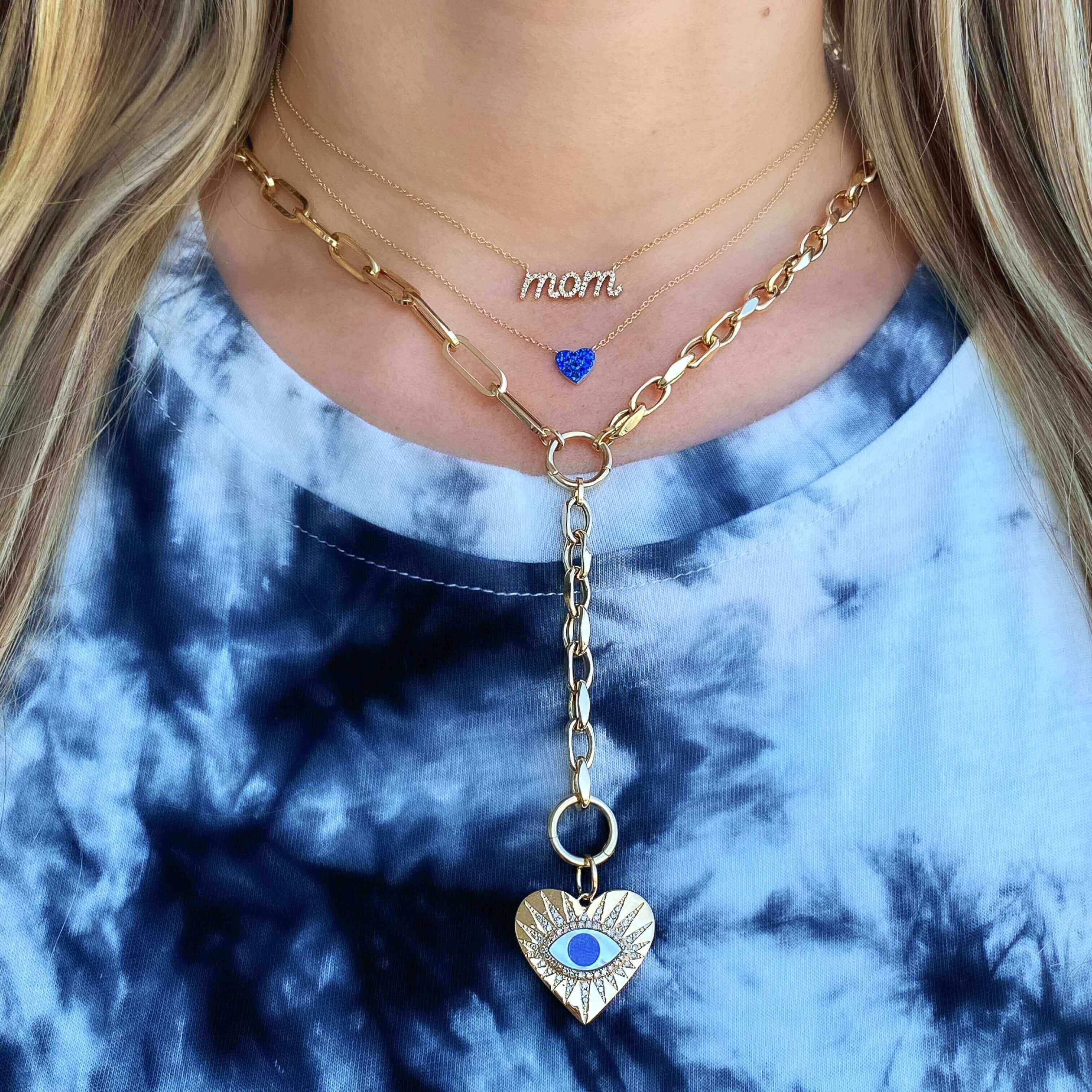 Woman wearing layered gold necklaces with "mom" pendant and heart-shaped charm showcasing our jewelry brand's unique designs