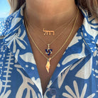 Woman wearing layered gold necklaces with Jewish symbols on a blue patterned shirt