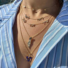 Woman wearing layered necklaces, gold star necklaces, and a blue Star of David necklace on a striped shirt, representing our jewelry brand.