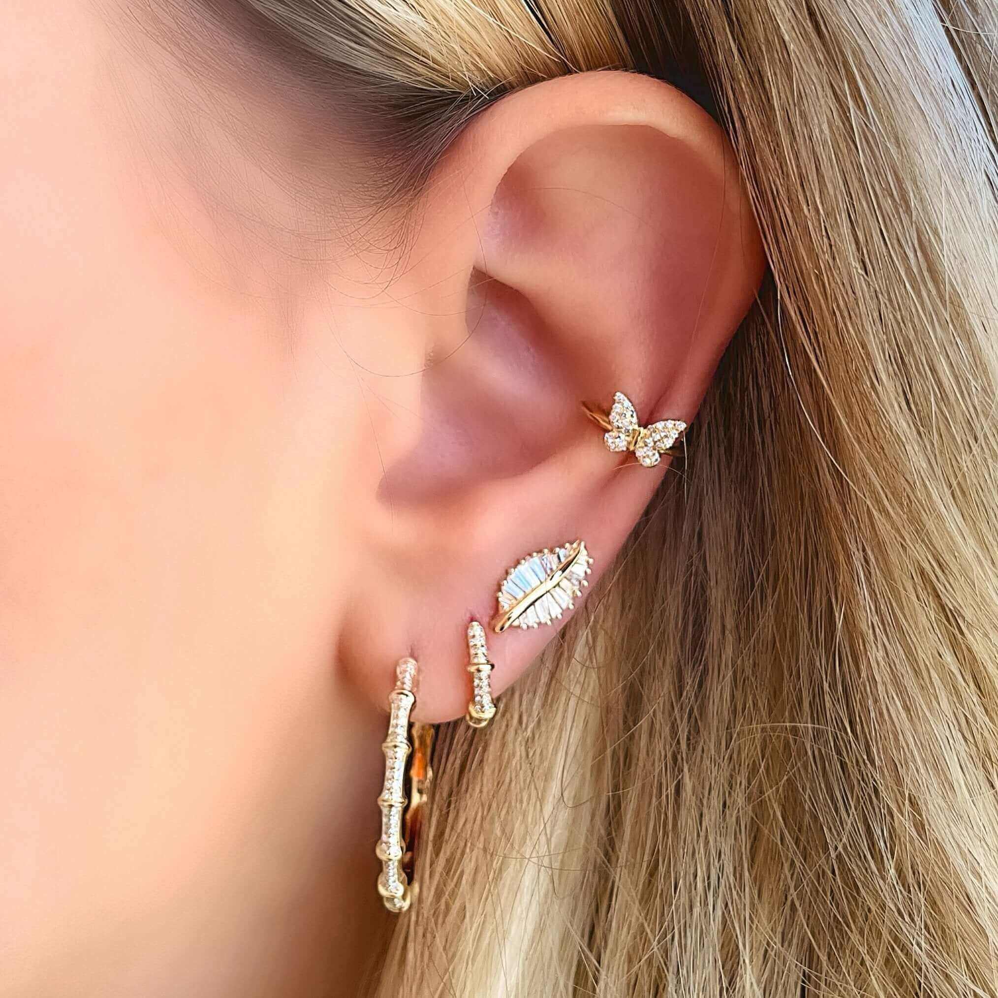 Woman wearing multiple gold earrings including a butterfly, leaf, and hoop design from our jewelry brand