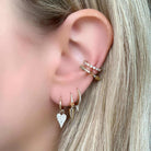 Woman wearing layered gold earrings with heart, arrow, and diamond designs by our jewelry brand.