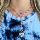 Woman wearing layered necklaces with gold chain, "mom" pendant, blue heart, and heart evil eye pendant from our jewelry brand.