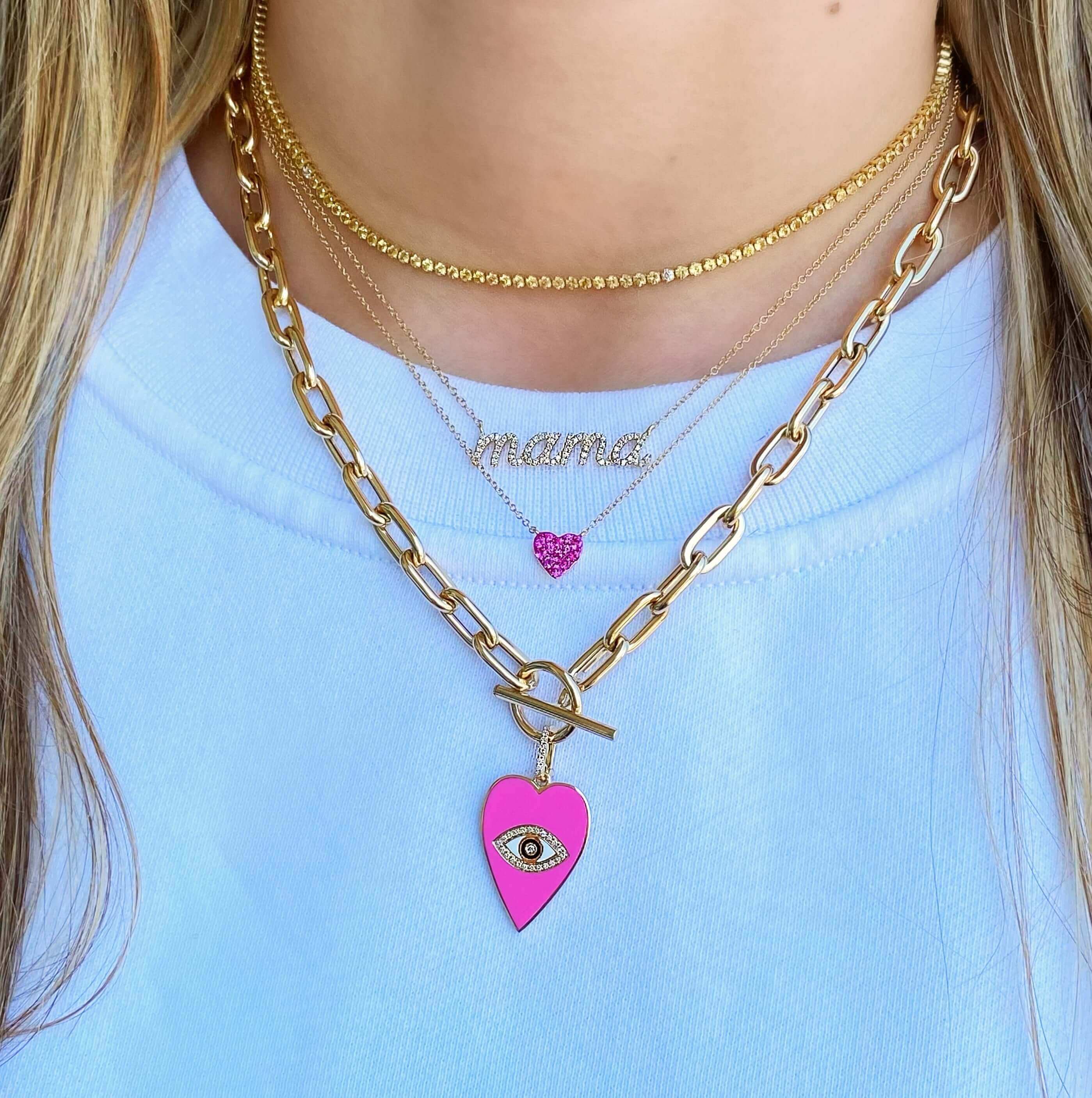 Woman wearing layered gold necklaces with a pink heart charm and eye design from our jewelry collection