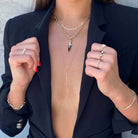 Woman wearing layered gold necklaces, stylish rings, and a chic black blazer, showcasing our jewelry brand's modern and elegant collection.