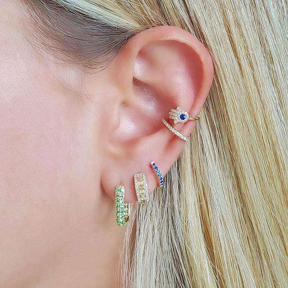 Close-up of ear with multiple gold and gemstone earrings from our premium jewelry collection showing a variety of colorful and elegant designs.