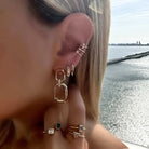 Woman wearing geometric earrings and stylish rings next to a serene water view