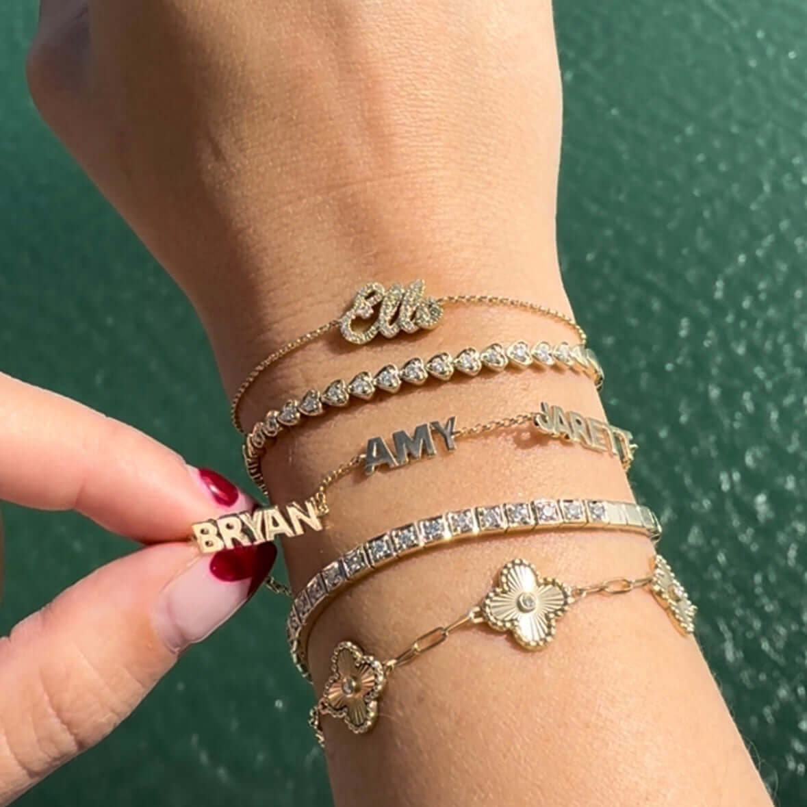 Multiple gold nameplate bracelets with personalized names displayed on a wrist, showcasing stylish and elegant designs.