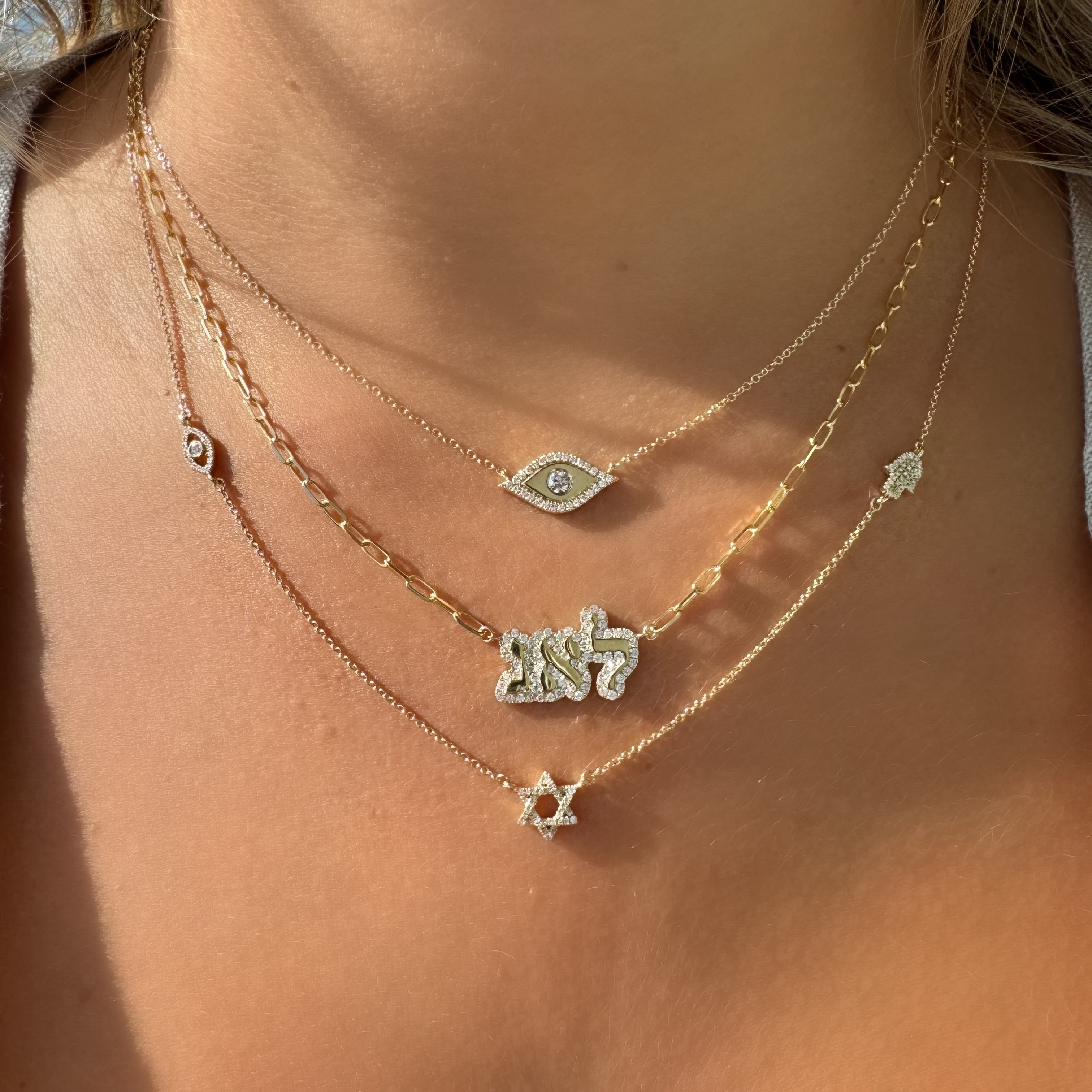 Four gold necklaces featuring a Hamsa, Evil Eye, and Star of David with diamonds worn elegantly on a woman's neck.