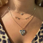 Woman wearing layered gold necklaces with Star of David and heart pendant, featuring intricate designs and sparkling accents.