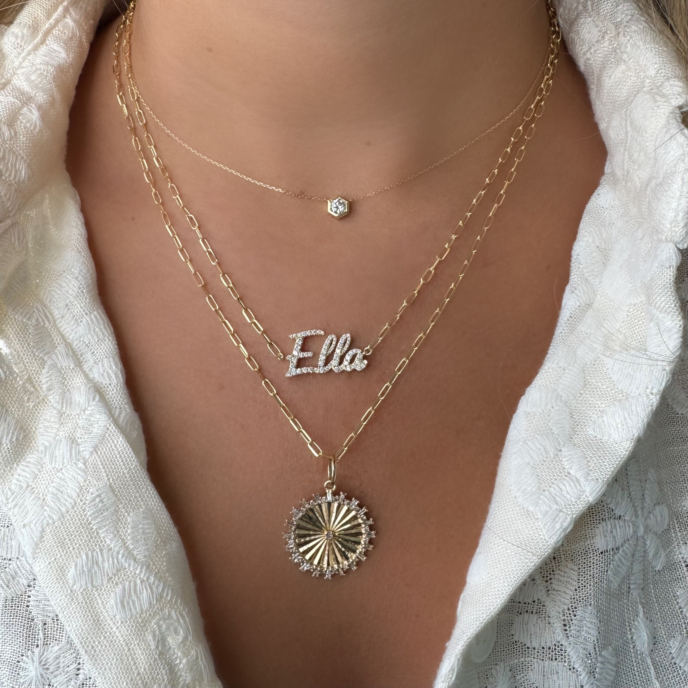 Woman wearing layered gold necklaces featuring a 14K gold medallion necklace charm with baguette diamonds, engraved "Ella."