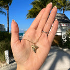 Hand displaying gold jewelry pendant necklace with palm trees and beach in the background