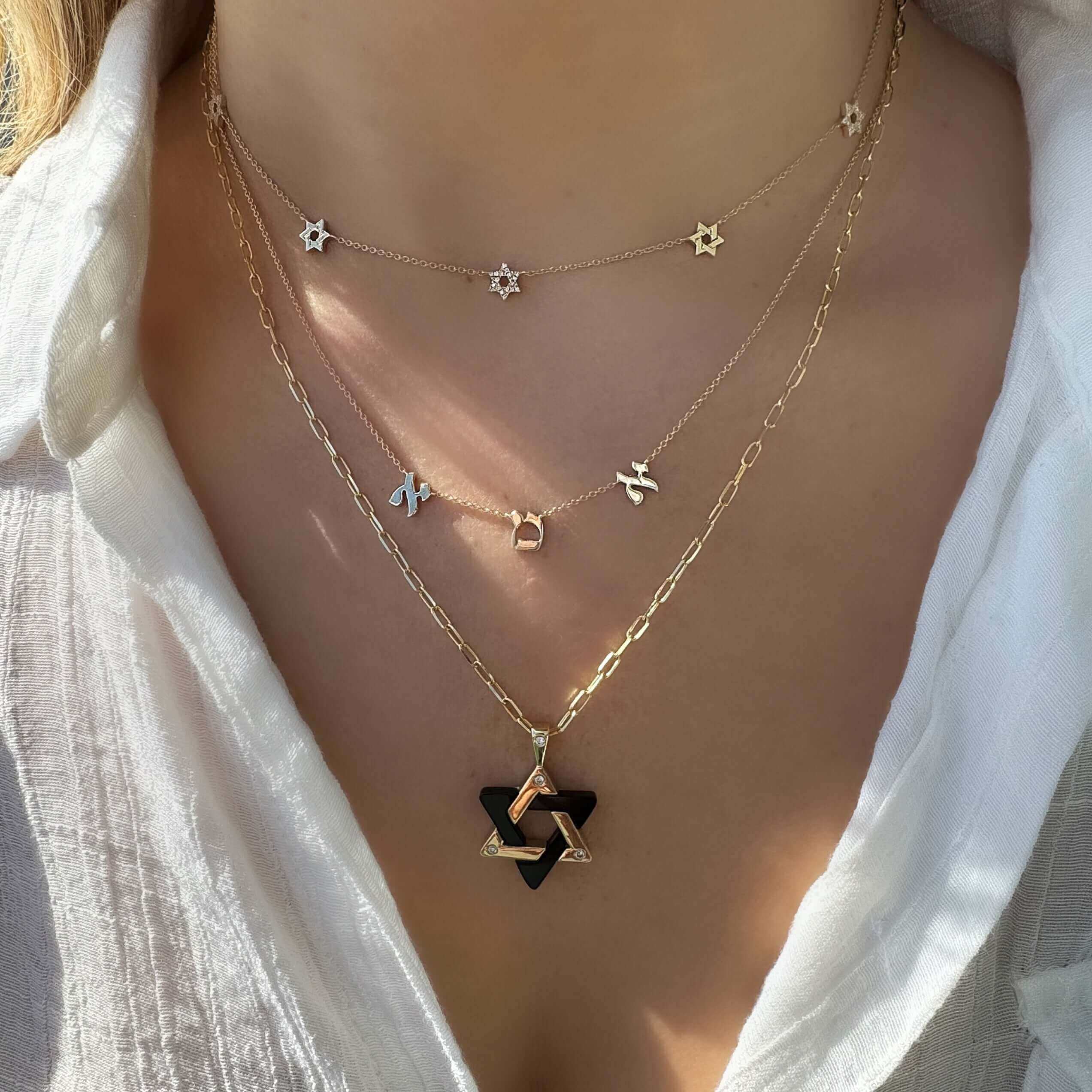 Woman wearing layered 14K gold necklaces, featuring Stars of David and hexagram pendants.