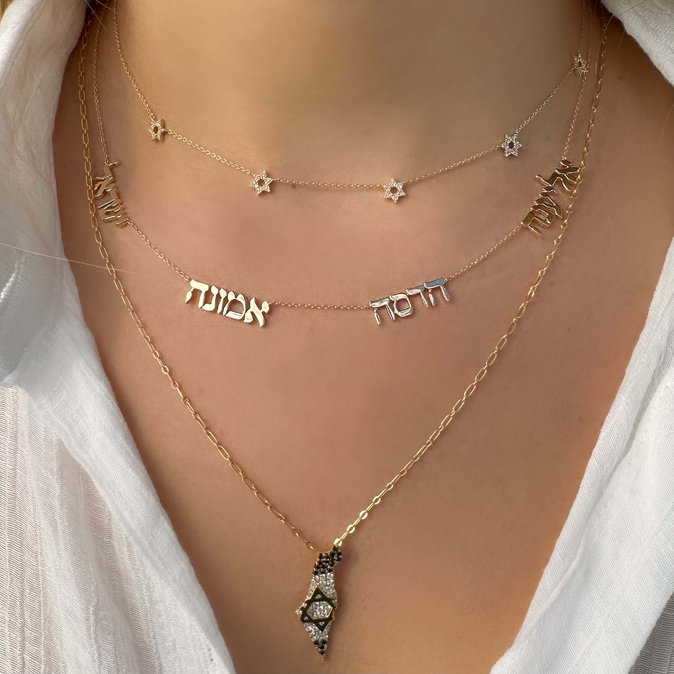 Woman wearing layered 14K gold necklaces with Star of David and Hebrew word pendants