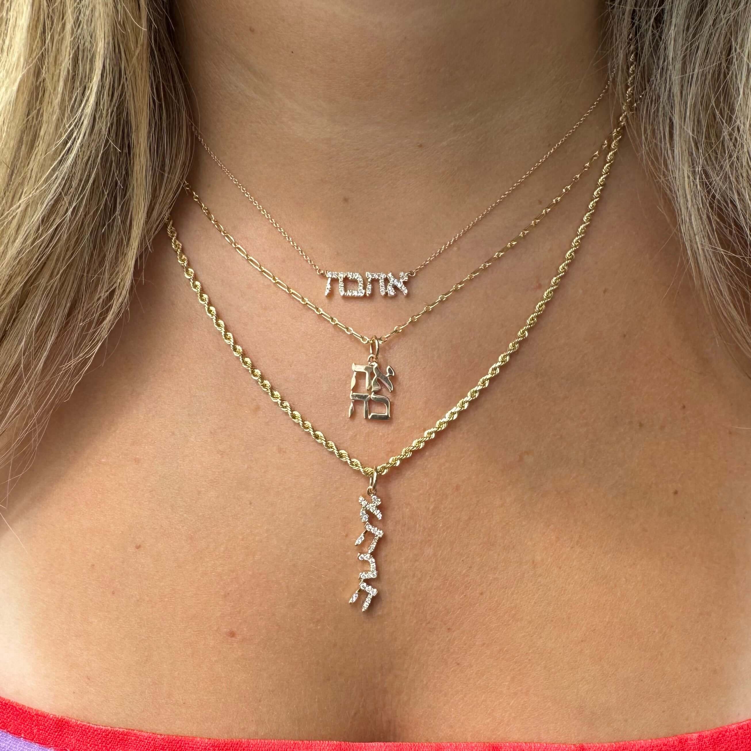 Woman wearing layered gold necklaces featuring unique Hebrew characters from a luxurious jewelry brand.