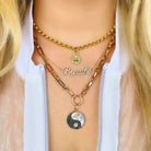 Woman wearing layered gold necklaces with "Breathe" pendant and yin-yang charm from our jewelry collection.